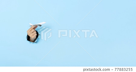Business Hand holds model plane from a hole in the wall on blue background. insurance travel concept. Panoramic image Business Hand holds model plane from a hole in the wall on blue background. insurance travel concept. Panoramic image 77883255