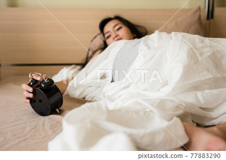 Asian woman stop clock alarm on bed. Time to wake up 77883290