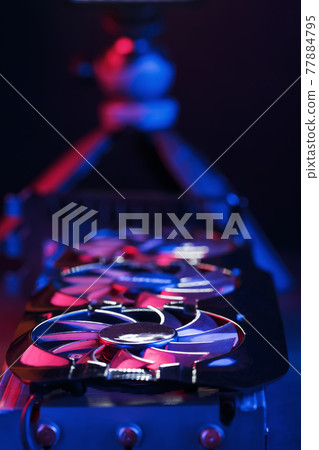 A graphics card with a row of fans with a cyanotic purple backlight in a futuristic design. A graphics card with a row of fans with a cyanotic purple backlight in a futuristic design. 77884795