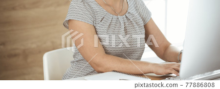 Unknown business woman working with computer while sitting at the desk in modern office, close-up. Middle aged female lawyer or auditor at work 77886808