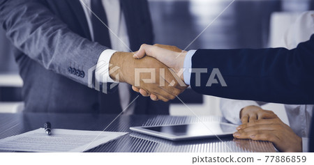 Handshake as successful negotiation ending, close-up. Unknown business people shaking hands after contract signing in modern office Handshake as successful negotiation ending, close-up. Unknown business people shaking hands after contract signing in modern office 77886859