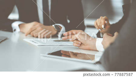 Unknown businessmen and woman sitting, working and discussing questions at meeting in modern office, close-up Unknown businessmen and woman sitting, working and discussing questions at meeting in modern office, close-up 77887587