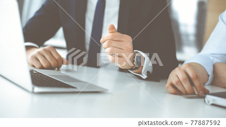 Unknown business people using laptop computer at the desk in modern office. Businessman or male entrepreneur is working with his colleague. Teamwork and partnership concept 77887592