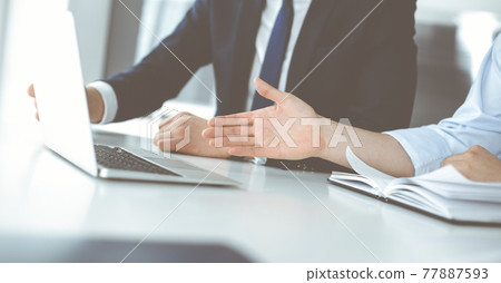 Unknown business people using laptop computer at the desk in modern office. Businessman or male entrepreneur is working with his colleague. Teamwork and partnership concept 77887593