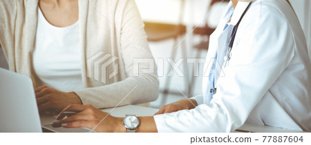 Unknown woman-doctor communicating with female patient in sunny clinic. Physician checks medical history record and exam results, close-up Unknown woman-doctor communicating with female patient in sunny clinic. Physician checks medical history record and exam results, close-up 77887604