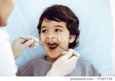 Cute arab boy sitting at dental chair with open mouth during oral checking up with doctor. Visiting dentist office. Stomatology concept 77887739