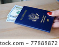 Female fingers holding American passport with dollar bills on wooden background. Travel concept. 77888872