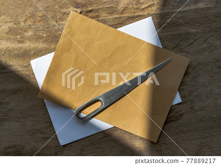 Envelope opener knife made of Stainless steel and two letter envelope on old wooden desk. 77889217