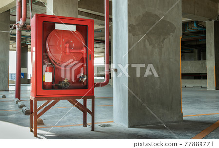 A red fire fighting equipment cabinet or fire extinguishing cabinet of fire protection set is located in condominium car parking. 77889771
