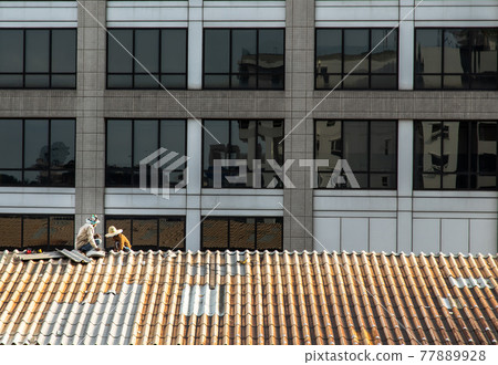 Two handyman workers repairing tiles on the damaged factory roof. Two handyman workers repairing tiles on the damaged factory roof. 77889928