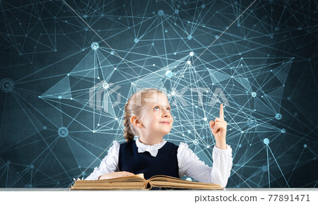 Smiling little girl sitting at desk with open book 77891471