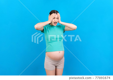 Beautiful young pregnant woman feeling head ache on colored background isolated. Stressed pregnant woman or mother problems Beautiful young pregnant woman feeling head ache on colored background isolated. Stressed pregnant woman or mother problems 77891674
