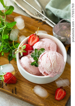 Homemade Organic Strawberry Ice Cream. Strawberry ice cream balls with mint leafon a light stone or slate table. 77891769