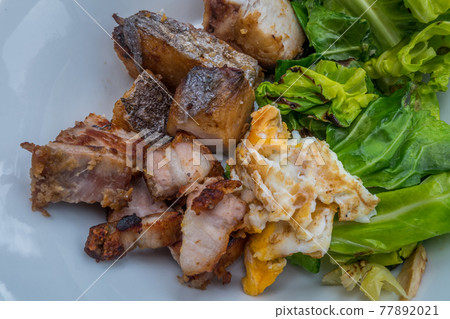 A dish with crispy pork, fish, fried eggs, and vegetables. A dish with crispy pork, fish, fried eggs, and vegetables. 77892021