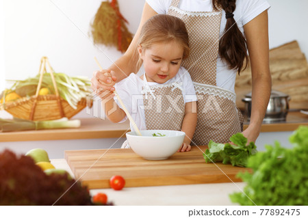 Happy woman and her daughter making healthy vegan salad and snacks for family feasting in sunny kitchen. Christmas, New year, Thanksgiving, Anniversary, Mothers Day. Healthy meal cooking concept Happy woman and her daughter making healthy vegan salad and snacks for family feasting in sunny kitchen. Christmas, New year, Thanksgiving, Anniversary, Mothers Day. Healthy meal cooking concept 77892475