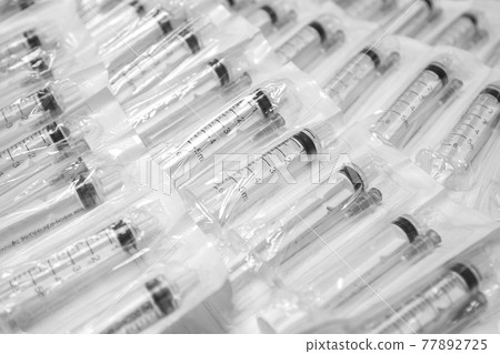 Medical syringes in a package. A bunch of unused, packaged syringes.Many new syringes lie strewn on a flat surface. 77892725