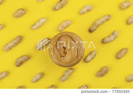 Bowl of peanut butter and scattered peanuts on yellow background Bowl of peanut butter and scattered peanuts on yellow background 77892893