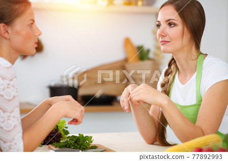 Two women friends choose the recipe and ingredients for a delicious meal in sunny kitchen. Vegetarian concept 77892993