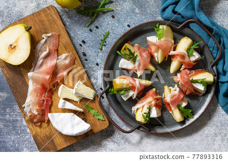 Summer snacks. Pear appetizer with jamon, arugula and brie cheese on a light stone table. Top view flat lay background. 77893316