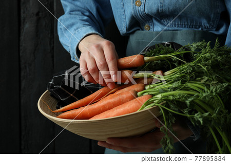 Woman hold bowl with carrot against dark wooden background Woman hold bowl with carrot against dark wooden background 77895884