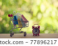 Red analog clock with shopping cart or a supermarket shopping basket and shopping bag on wood table. Fast delivery, time value of money concept : depicts the time is of the essence in our daily life. 77896217