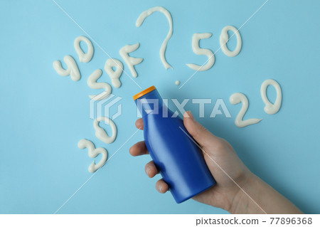 Female hand holds sunscreen on blue background with text SPF? Female hand holds sunscreen on blue background with text SPF? 77896368