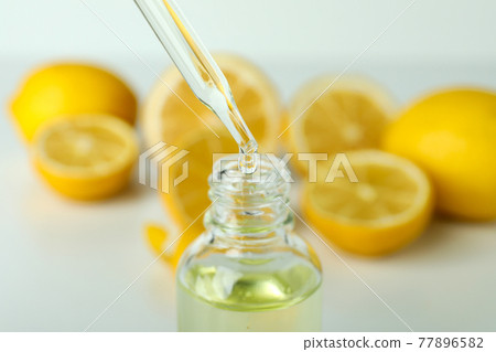 Pipette dripping oil in bottle against fresh lemons Pipette dripping oil in bottle against fresh lemons 77896582