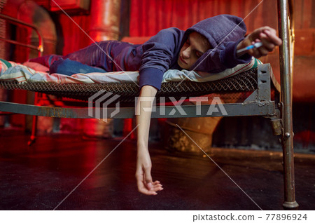 Drug addict woman sleeps on bed in den 77896924