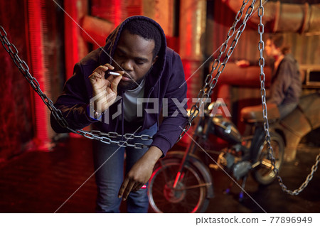Drug addict man smokes a cigarette in den Drug addict man smokes a cigarette in den 77896949