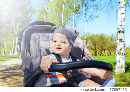 Happy baby boy in stroller in park. Happy baby boy in stroller in park. 77897453