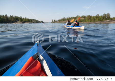 Tourists in kayaks walk on the smooth water of the lake against the backdrop of rocky shores 77897507