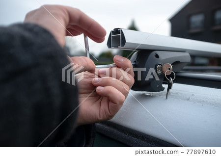 Hands with a screwdriver installs attachments for the trunk or cargo box on the roof of the car. Hands with a screwdriver installs attachments for the trunk or cargo box on the roof of the car. 77897610