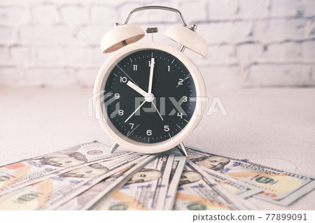 Close up of 100 dollar cash and old alarm clock on table Close up of 100 dollar cash and old alarm clock on table 77899091