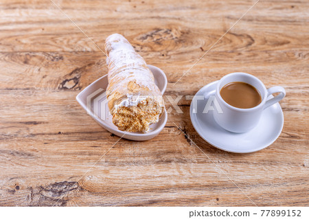 A cup of coffee next to delicious aromatic puff pastry cone with protein cream 77899152