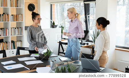 Three confident diverse businesswomen brainstorming project, standing in office 77899328