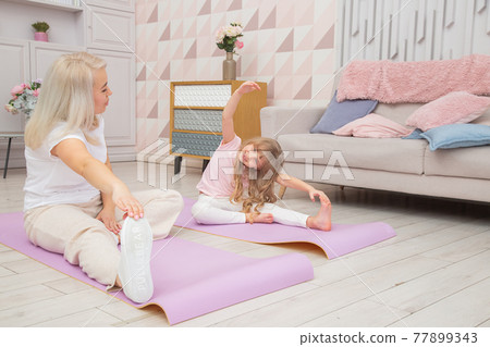 Smiling blond mother on yoga mat with cute playful daughter do exercises. 77899343