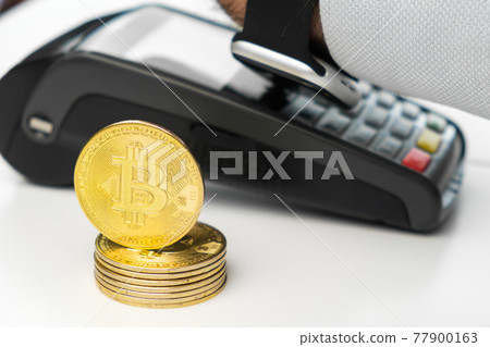 Golden bitcoin coins next to payment terminal on the table. Cryptocurrency for payment concept. Golden bitcoin coins next to payment terminal on the table. Cryptocurrency for payment concept. 77900163