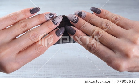 Female hand with beautiful manicure nails in the form of chocolate candies, holding an unrolled bar Female hand with beautiful manicure nails in the form of chocolate candies, holding an unrolled bar 77900618