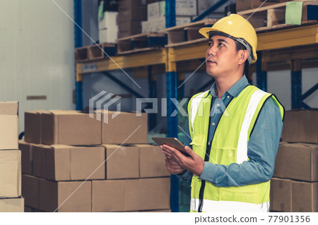Asian warehouse worker checking packages in storehouse Asian warehouse worker checking packages in storehouse 77901356