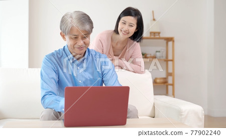 Middle couple using a computer in the living room Middle couple using a computer in the living room 77902240