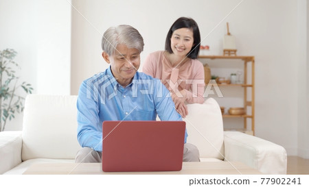Middle couple using a computer in the living room Middle couple using a computer in the living room 77902241