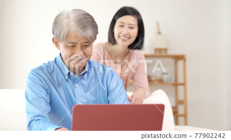 Middle couple using a computer in the living room Middle couple using a computer in the living room 77902242