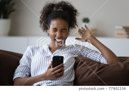 Overjoyed young african woman celebrating online lottery win. Overjoyed young african woman celebrating online lottery win. 77902336