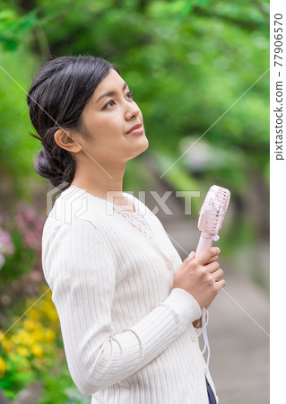 A businesswoman cooling off with a handheld fan amid the fresh greenery A businesswoman cooling off with a handheld fan amid the fresh greenery 77906570