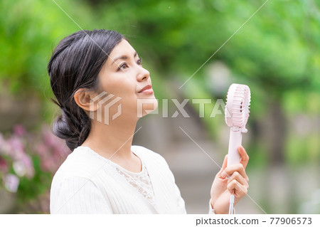 A businesswoman cooling off with a handheld fan amid the fresh greenery A businesswoman cooling off with a handheld fan amid the fresh greenery 77906573