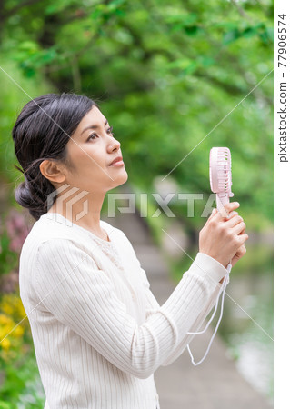 A businesswoman cooling off with a handheld fan amid the fresh greenery A businesswoman cooling off with a handheld fan amid the fresh greenery 77906574