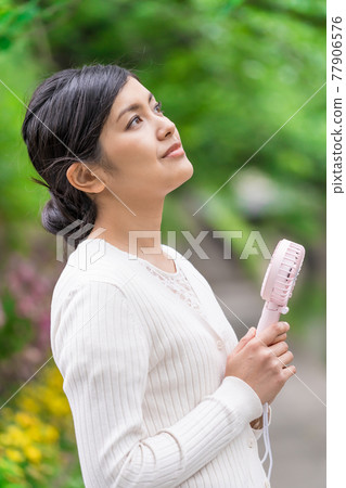 一位女商人在新鮮的綠色植物中拿著一把方便的風扇納涼 77906576