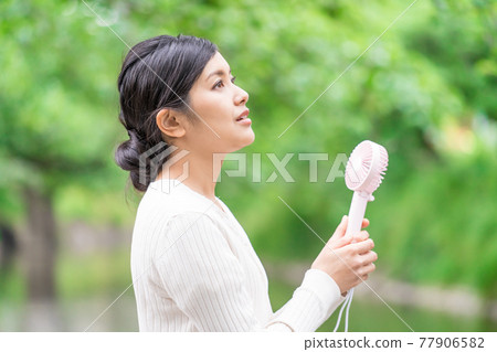 一位女商人在新鮮的綠色植物中拿著一把方便的風扇納涼 77906582