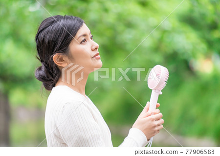 一位女商人在新鮮的綠色植物中拿著一把方便的風扇納涼 77906583