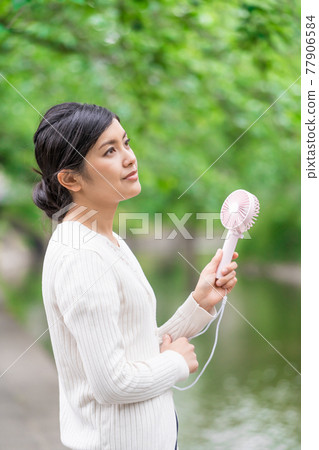 A businesswoman cooling off with a handheld fan amid the fresh greenery 77906584